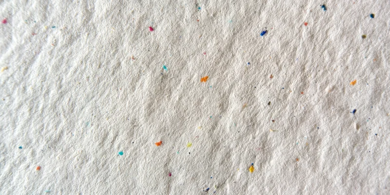 Close-up of textured off-white paper surface with scattered multicolored specks