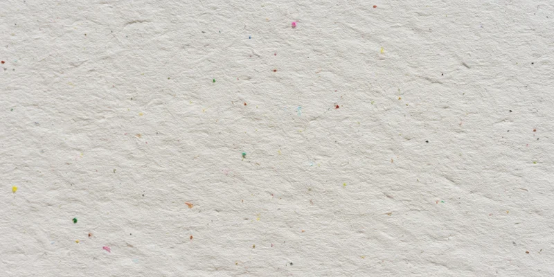 Close-up of textured off-white paper surface with scattered multicolored specks
