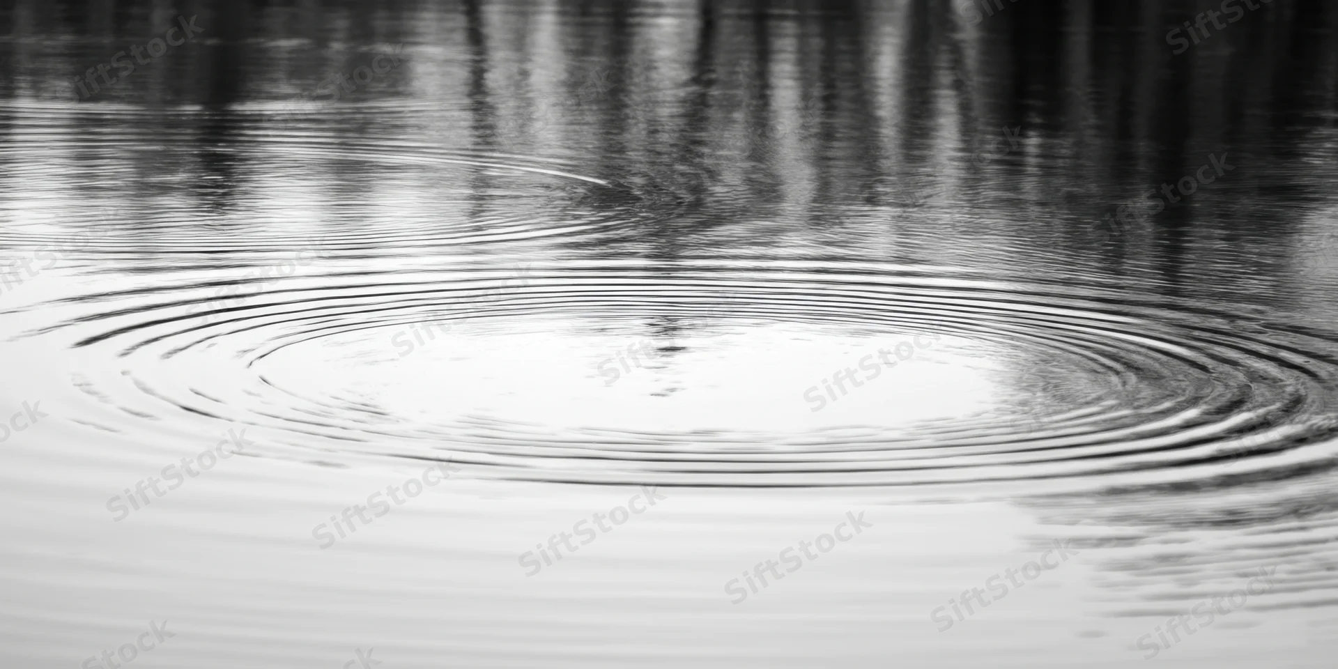 Concentric ripples spreading across calm water surface with reflections