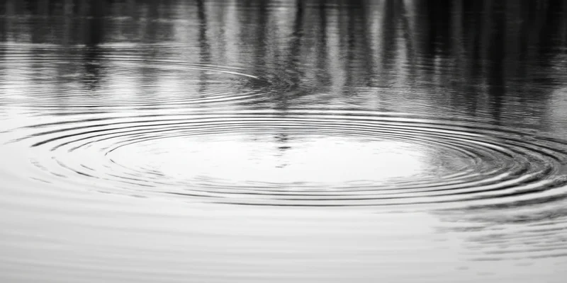 Concentric ripples spreading across calm water surface with reflections