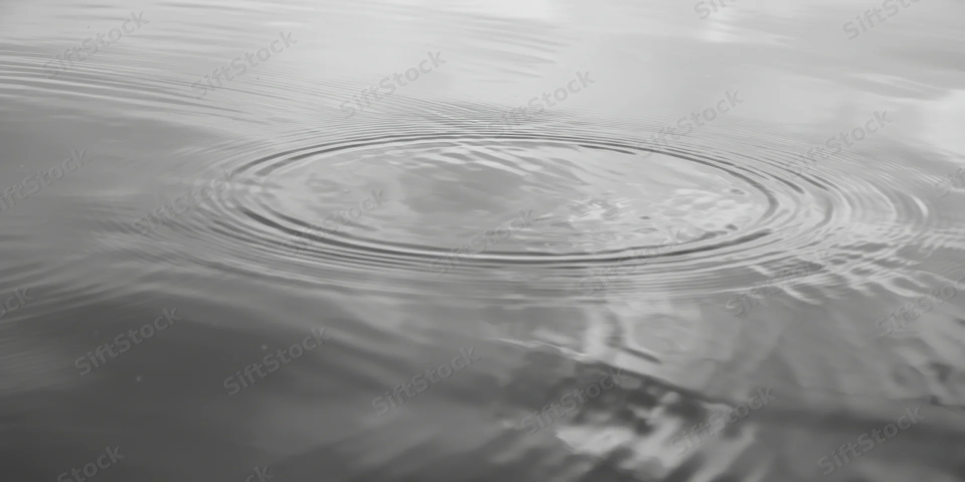 Concentric ripples spreading across calm water surface with reflections and subtle light variations