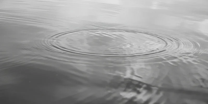 Concentric ripples spreading across calm water surface with reflections and subtle light variations