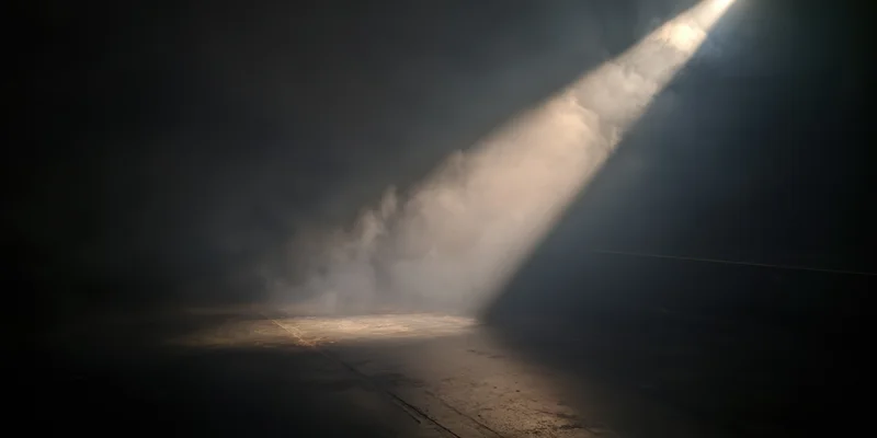 Single beam of light cutting through thick fog on a dark stage