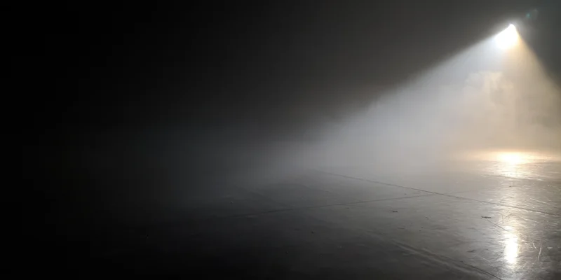 Single spotlight beam cutting through thick fog on a dark stage floor