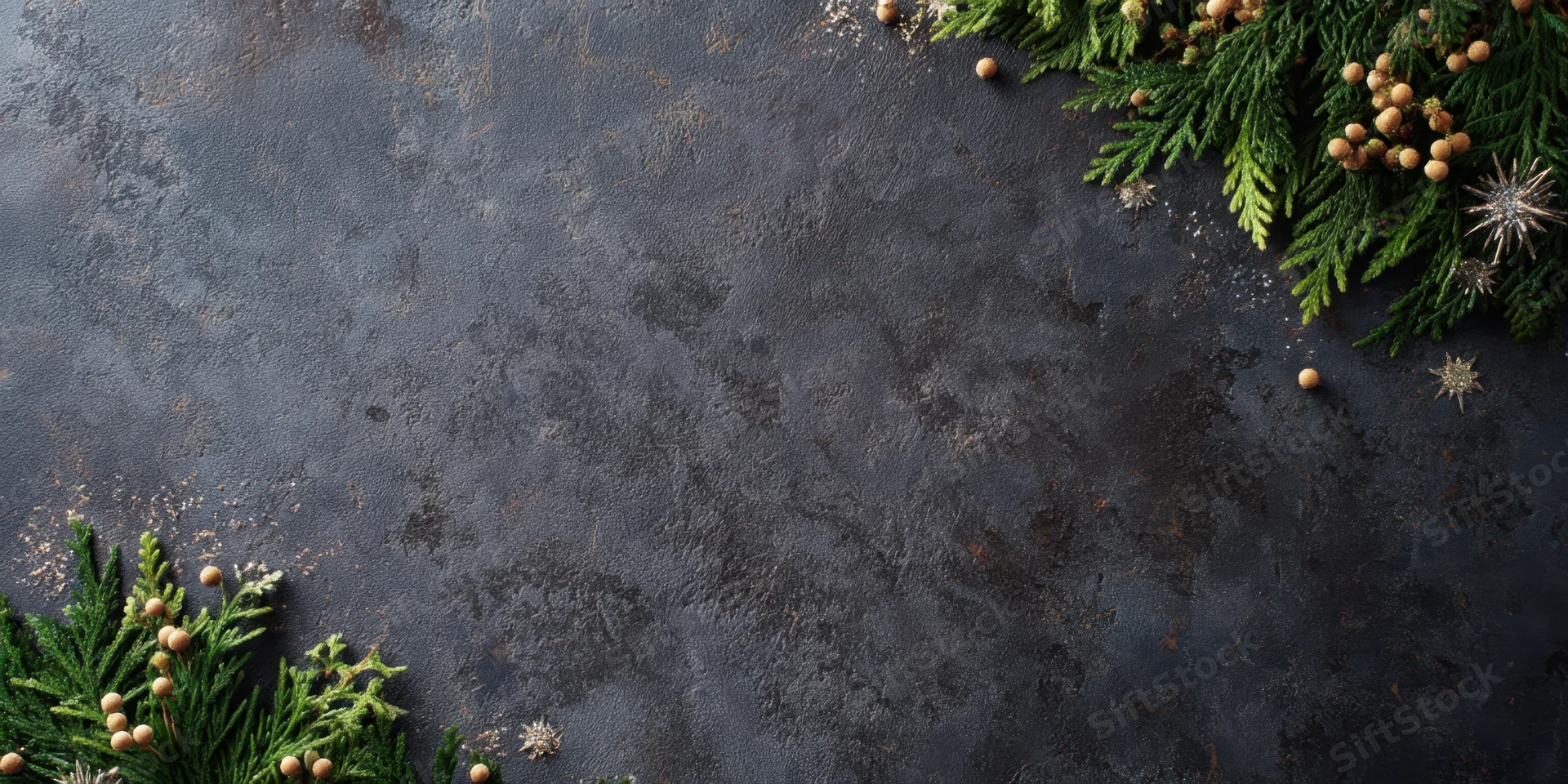 Evergreen branches and festive ornaments arranged in corners on dark textured slate background with copyspace