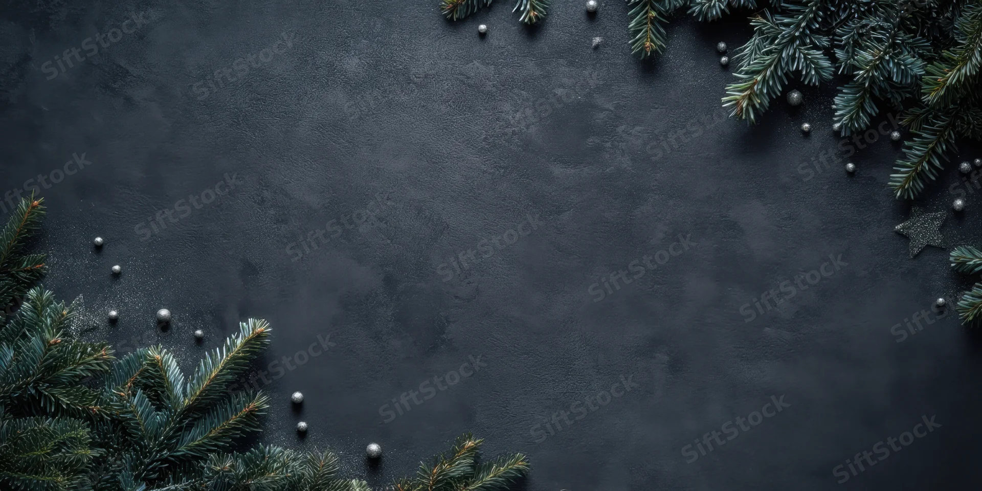 Evergreen branches and silver ornaments arranged in a frame on a dark textured slate background with copyspace