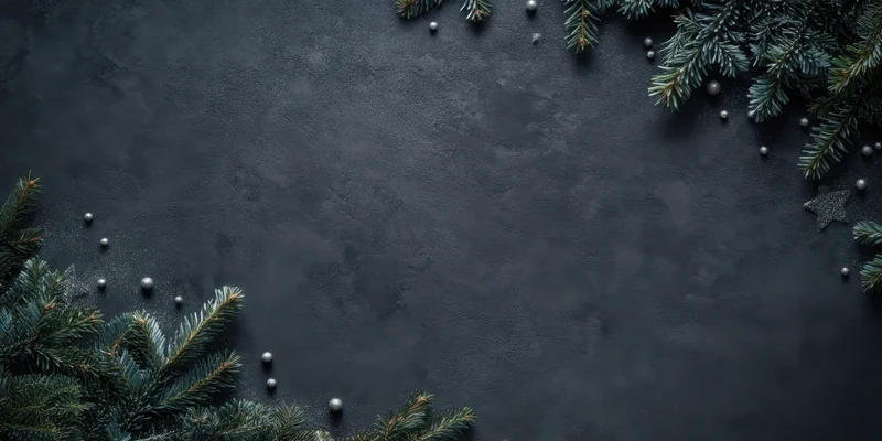 Evergreen branches and silver ornaments arranged in a frame on a dark textured slate background with copyspace