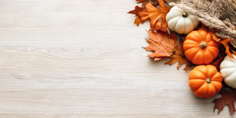 Small pumpkins and autumn leaves arranged on a light wooden surface with copyspace