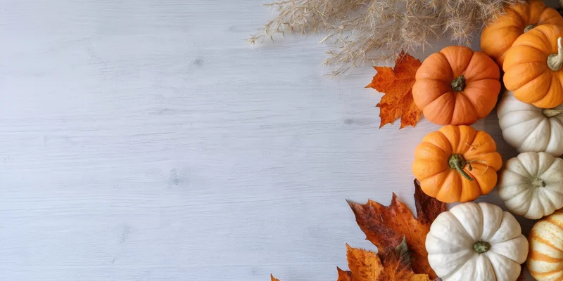 Small pumpkins and autumn leaves arranged on a light wooden surface with copyspace