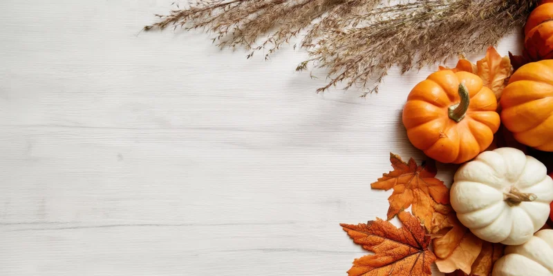 Small pumpkins and autumn leaves arranged on a light wooden surface with copyspace