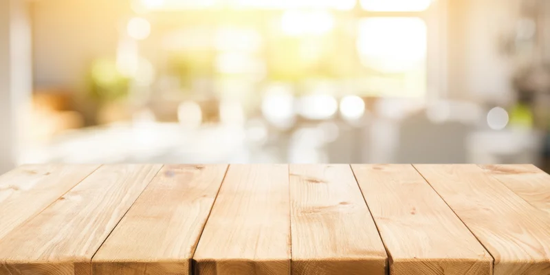 Light wooden tabletop in foreground with blurred interior background