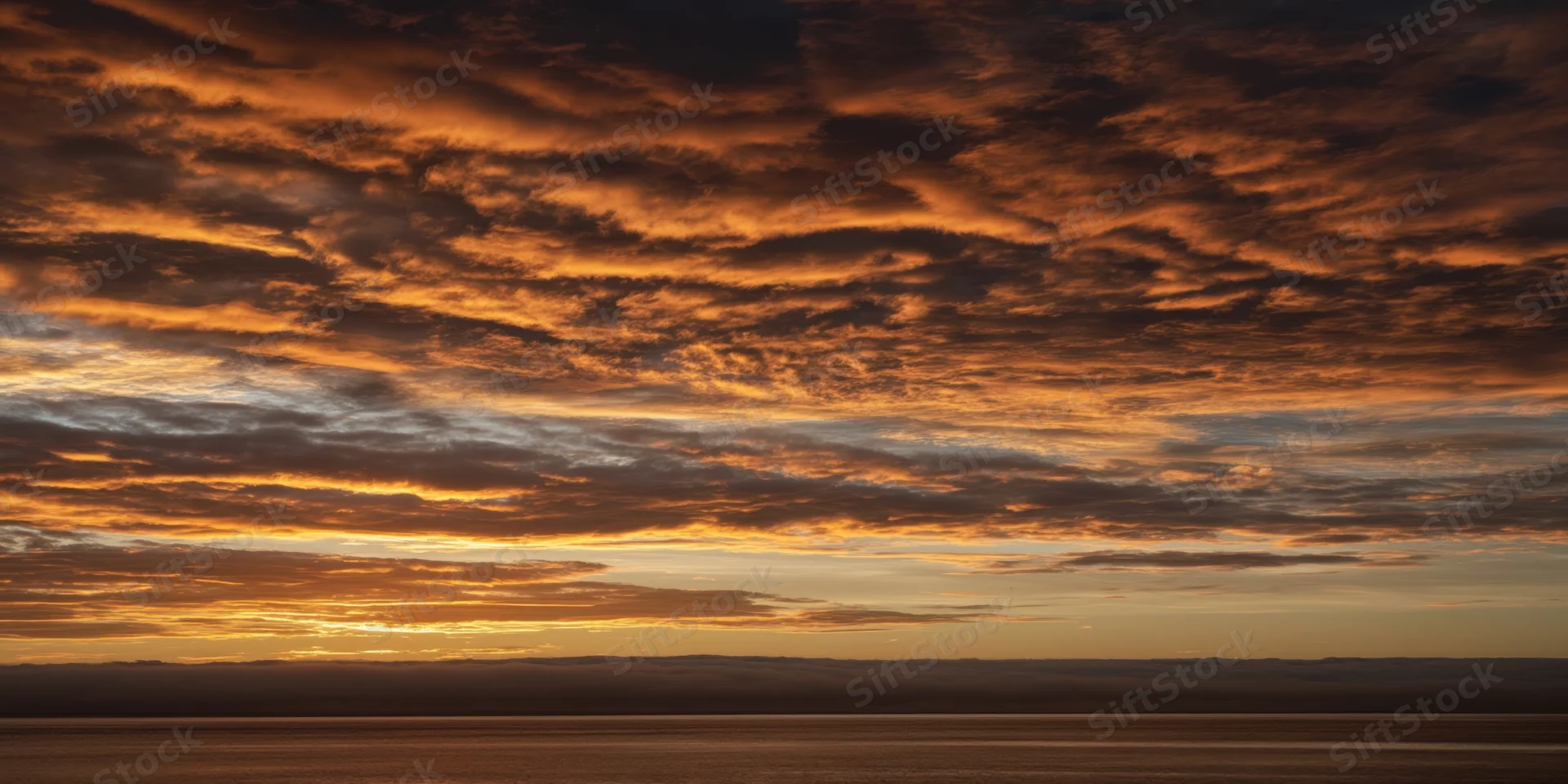 Textured orange-brown clouds at sunset over calm water with distant mountain silhouette