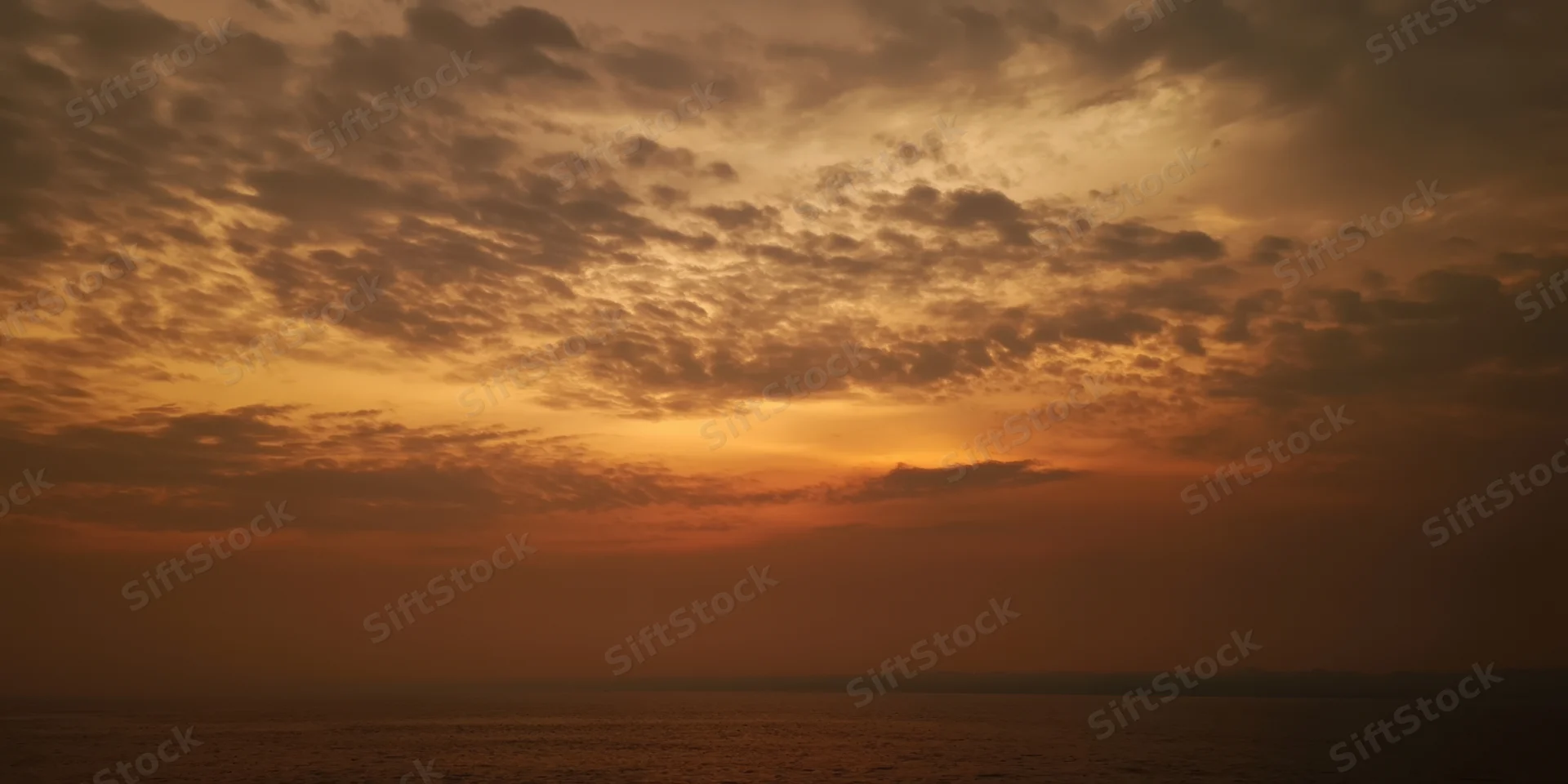 Moody sunset sky with textured orange-brown clouds over calm ocean at dusk