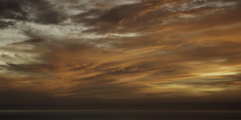Moody sunset sky with textured orange-brown clouds over calm ocean and distant horizon