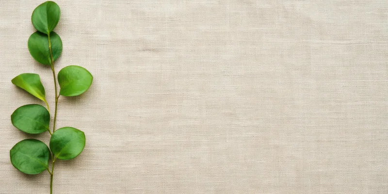 Slender green leafy branch arranged vertically on beige woven fabric background