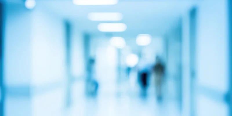 Blurred view of a cool blue-toned office hallway with diffused ceiling lights and indistinct figures moving in the distance