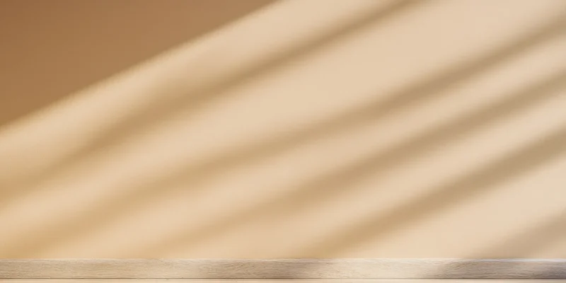 Warm beige wall with soft diagonal shadows from daylight, featuring a wooden plank surface at the bottom