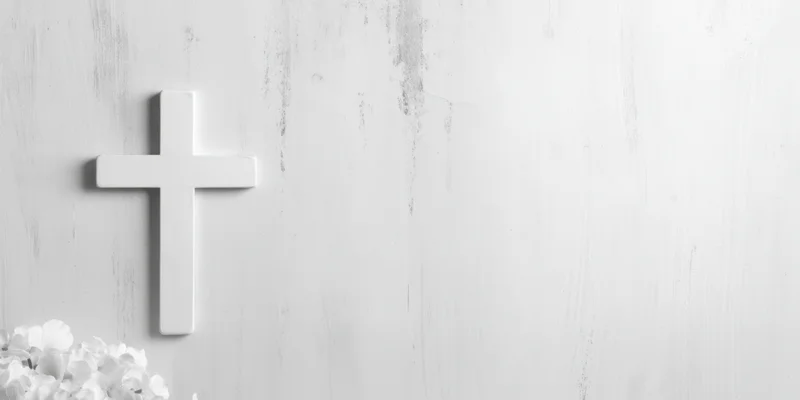 White cross mounted on a light weathered wall with white flowers at the base