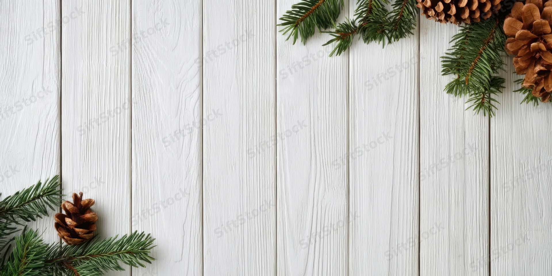 Pine branches and pinecones arranged in corners on a white wooden surface with visible grain