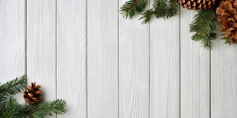Pine branches and pinecones arranged in corners on a white wooden surface with visible grain