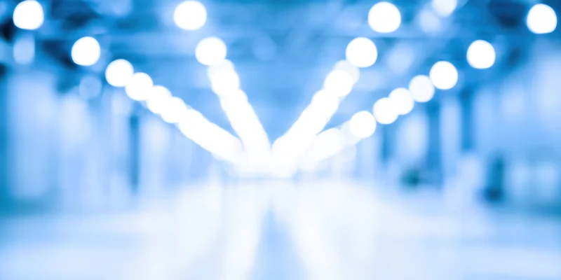 Blurred industrial interior with bright overhead lights arranged in a symmetrical row along the ceiling, reflecting on a glossy floor