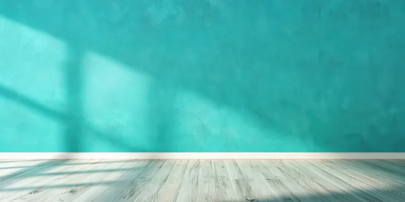 Empty studio interior with turquoise textured wall and pale wooden floor, sunlight casting window shadows