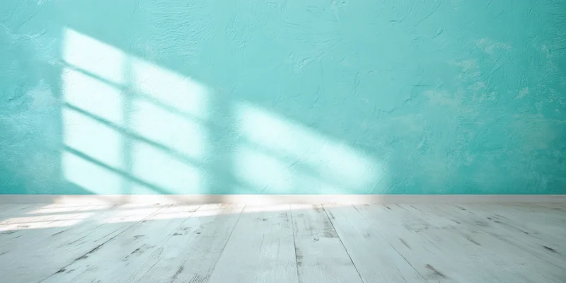 Empty studio interior with turquoise textured wall and pale wooden floor, natural light casting window shadow