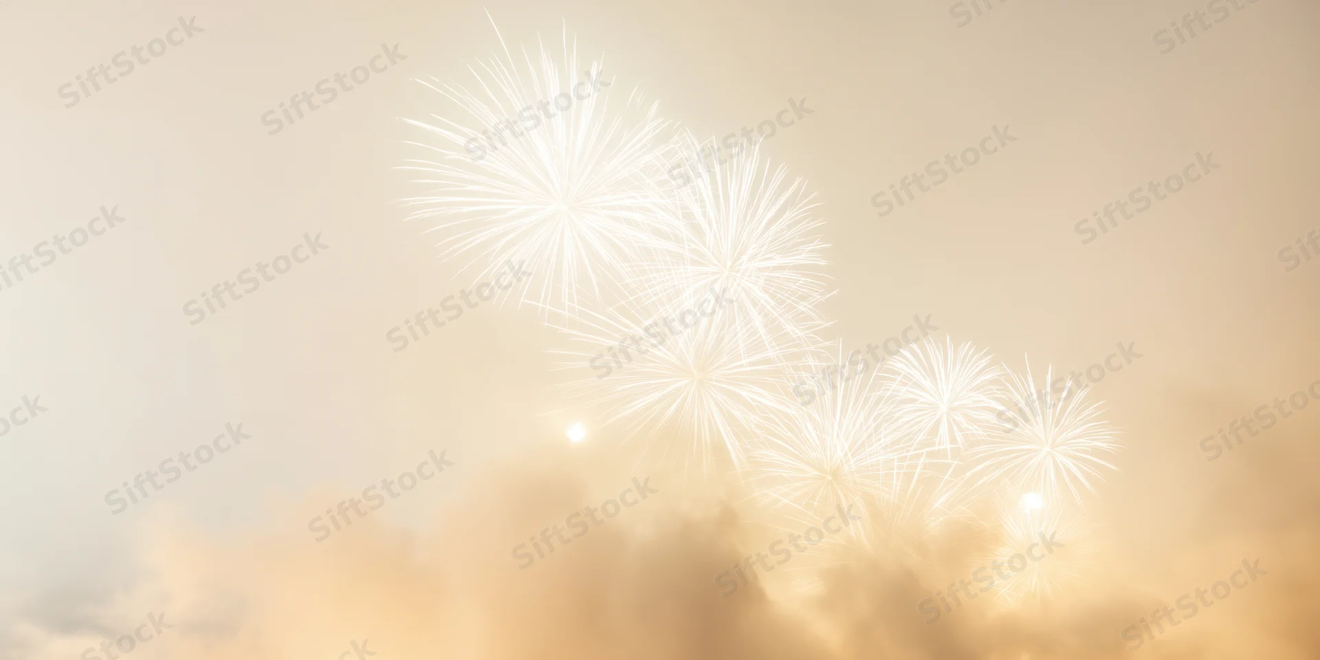 White fireworks bursting in a hazy night sky with golden glow and smoke clouds