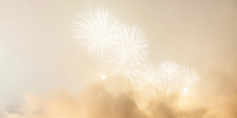 White fireworks bursting in a hazy night sky with golden glow and smoke clouds