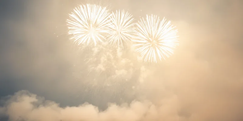 White fireworks bursting in a hazy night sky above clouds