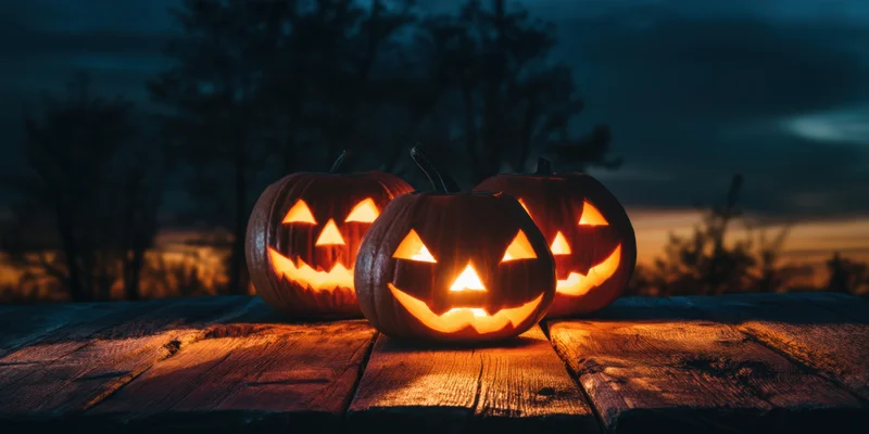 Three glowing jack-o-lanterns arranged on a weathered wooden table outdoors at twilight