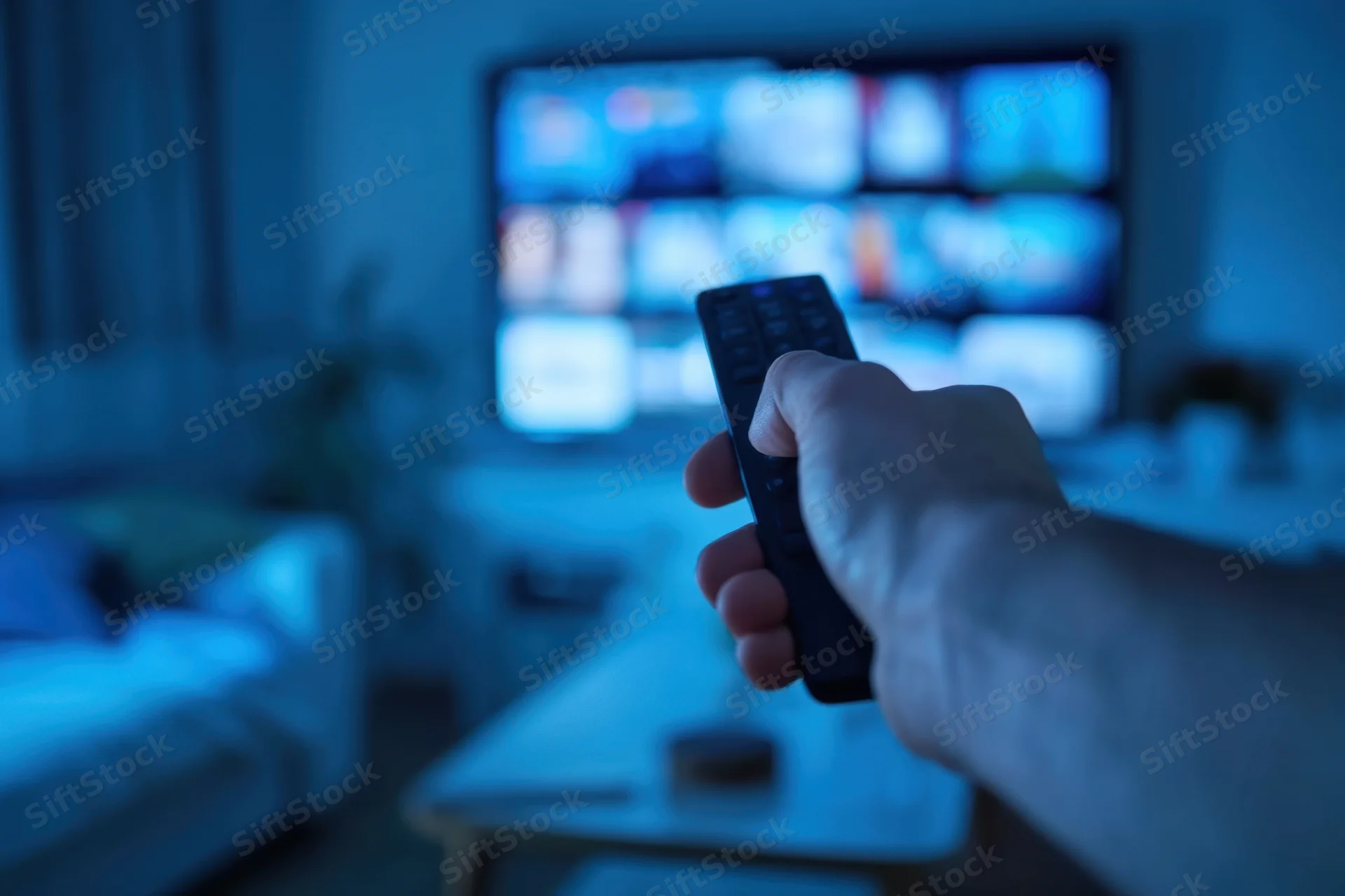 Hand gripping remote pointing at smart tv in dimly lit living room