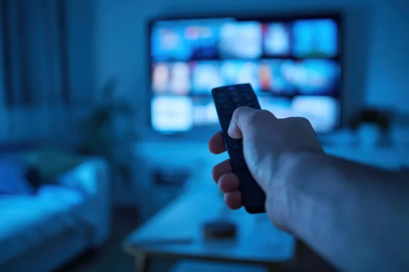 Hand gripping remote pointing at smart tv in dimly lit living room