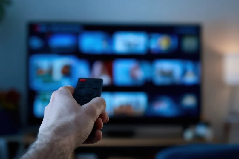 Hand gripping remote pointing at smart tv streaming interface in living room