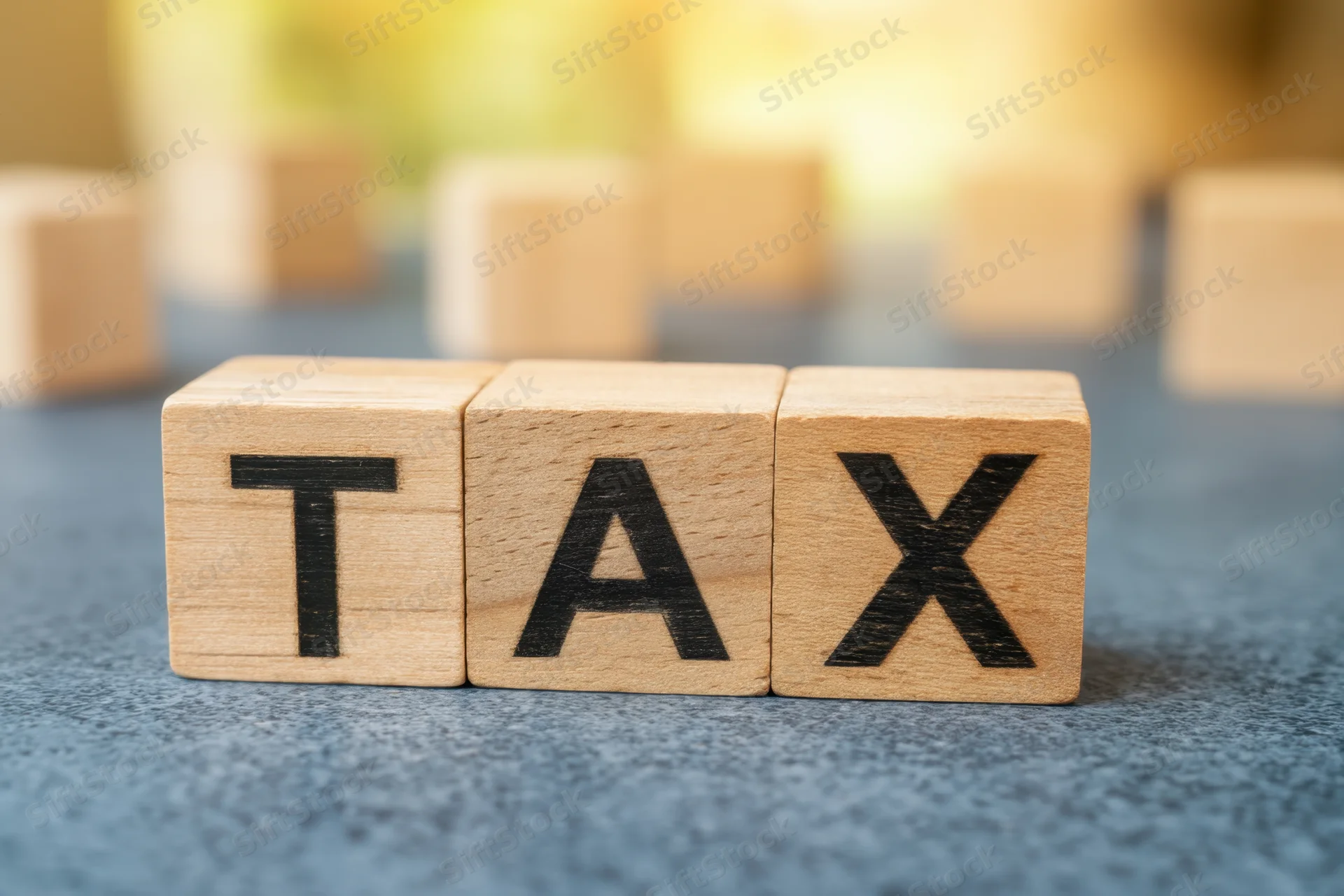 Wooden blocks spelling tax arranged in a row on a blue textured surface with blurred background