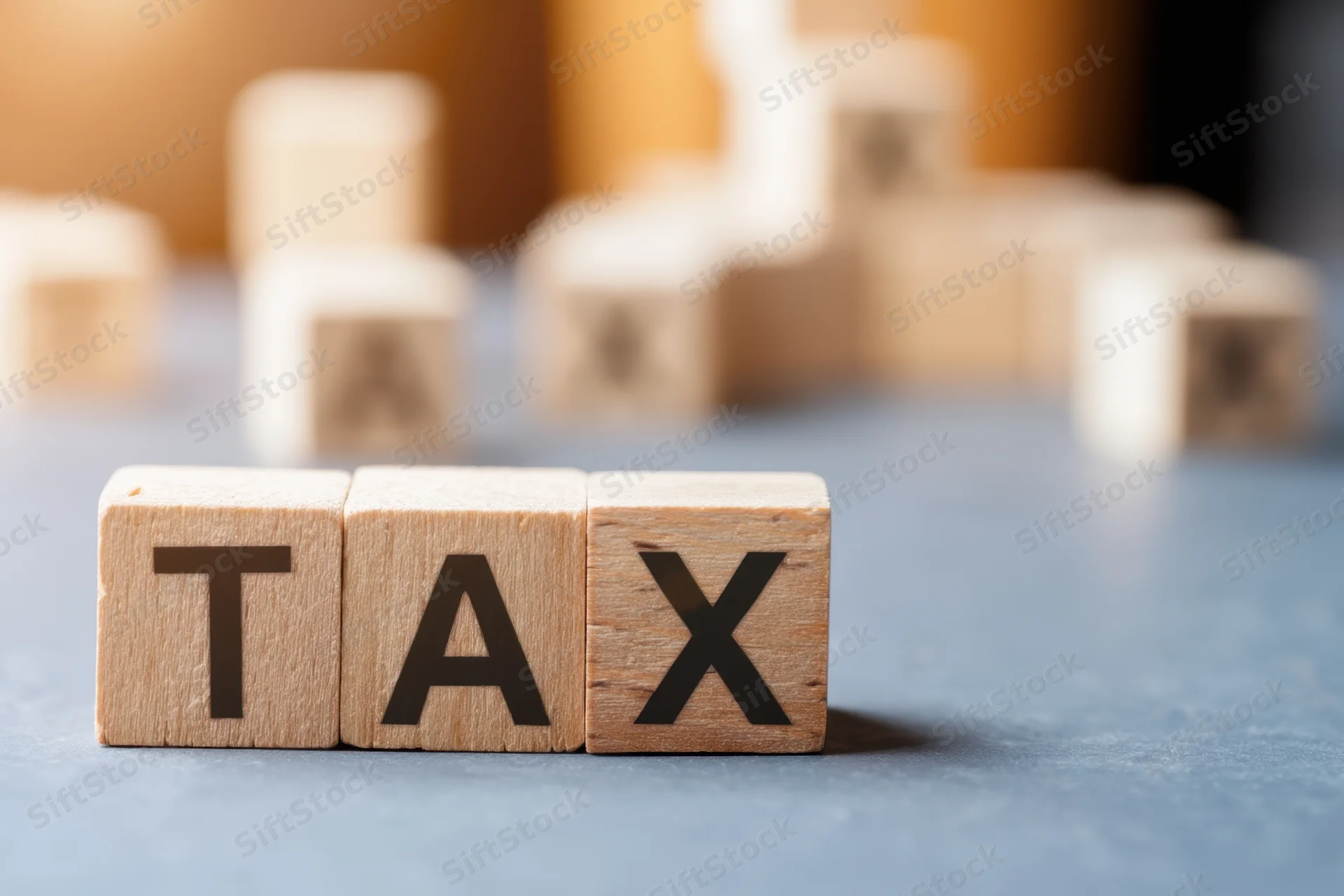 Wooden blocks spelling tax arranged on a blue-gray surface with blurred background