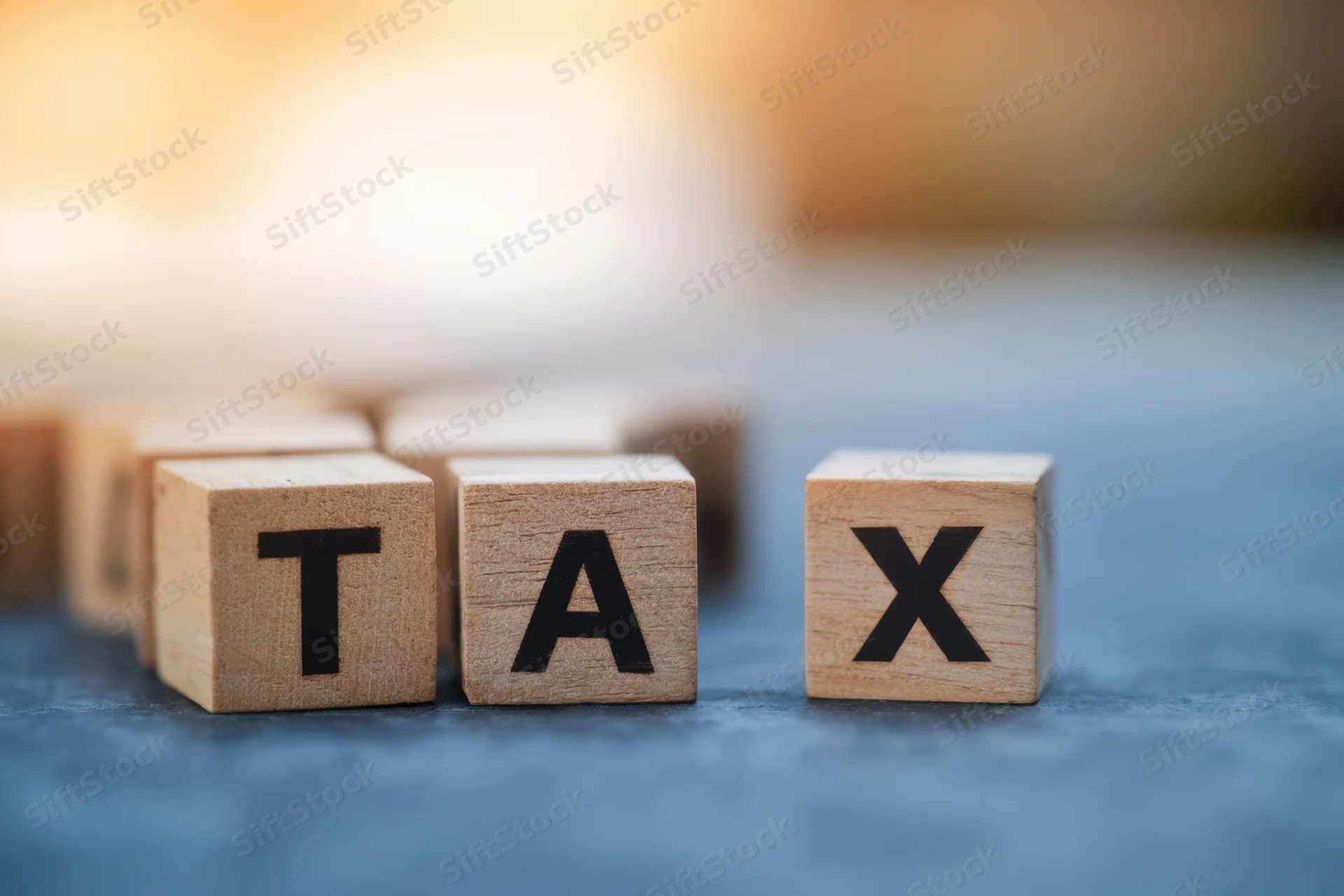 Wooden letter blocks spelling tax arranged in a row on a blue surface with blurred background