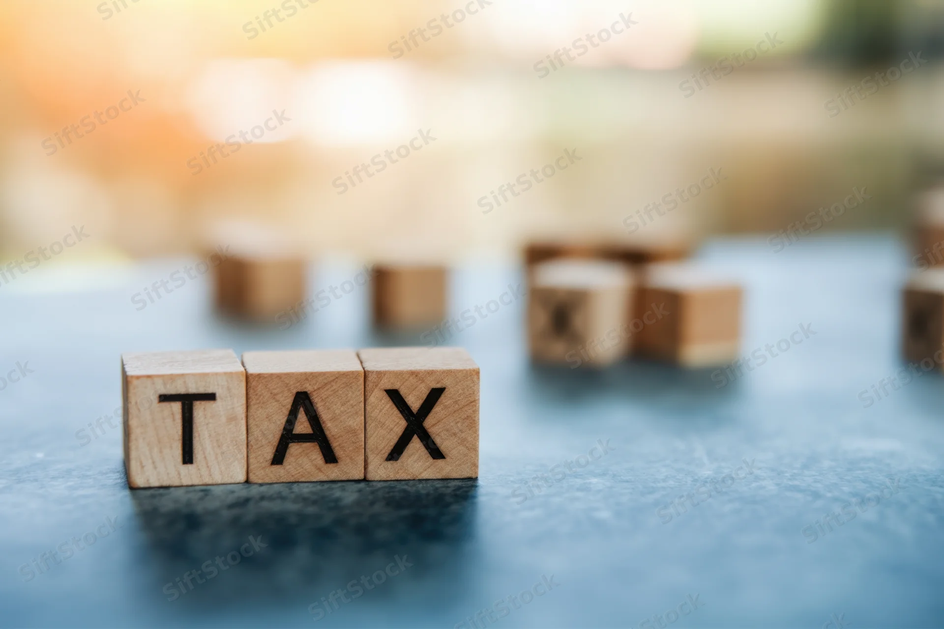 Wooden blocks spelling tax arranged in a row on a blue surface with blurred background