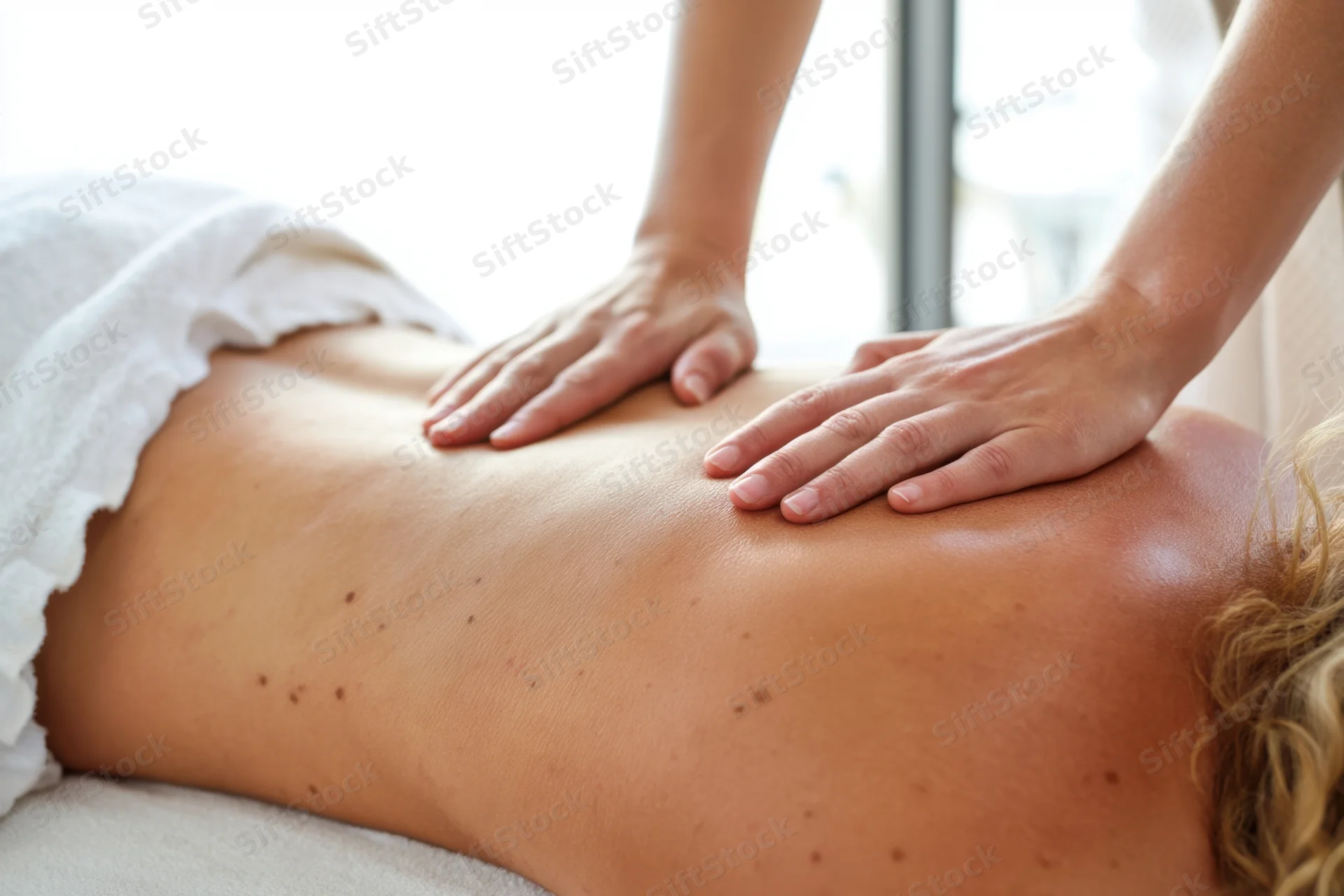 Massage therapist applying firm pressure to client's bare back in spa setting