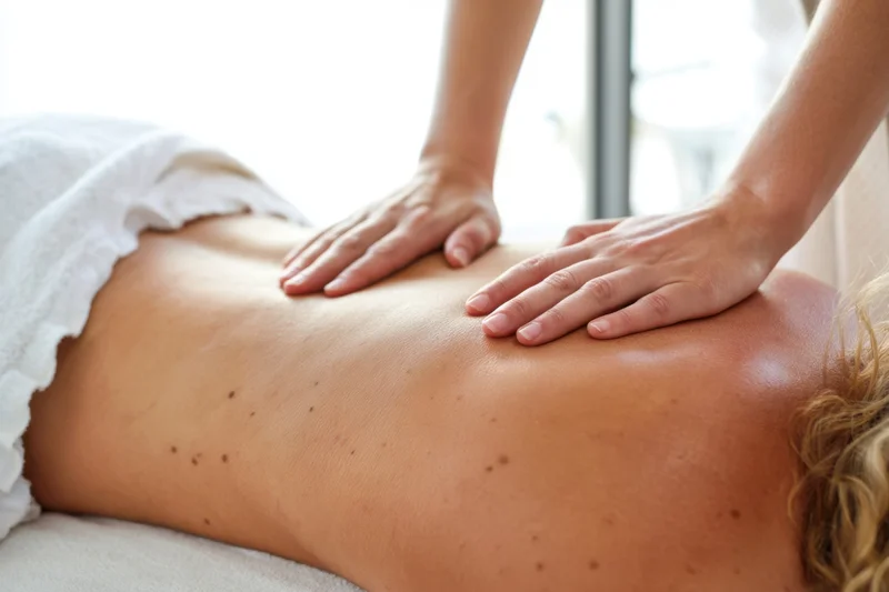 Massage therapist applying firm pressure to client's bare back in spa setting