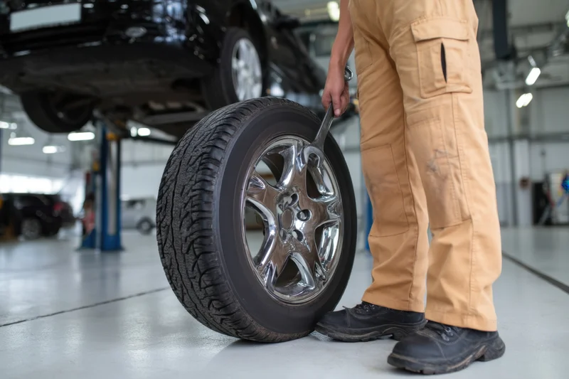 Mechanic using wrench on chrome alloy wheel and tire in automotive garage