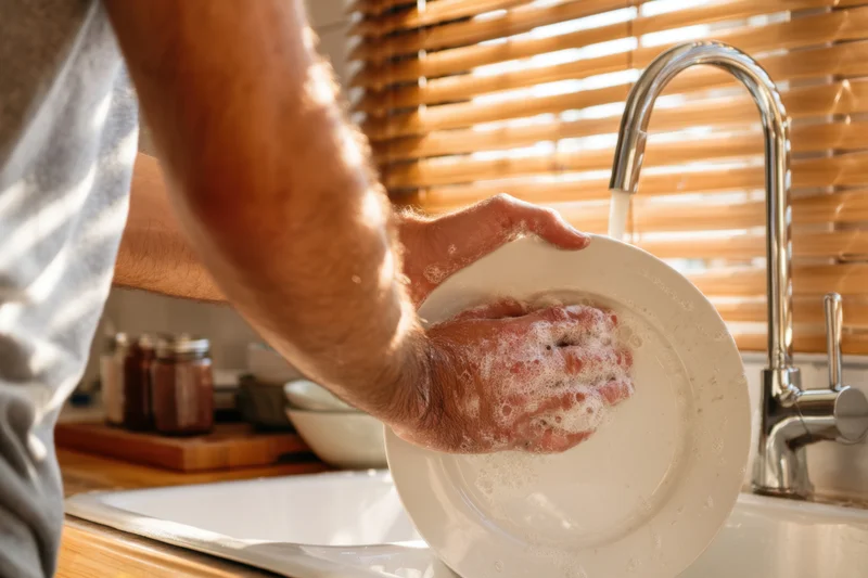 Man washing a white plate with soapy hands in a kitchen sink