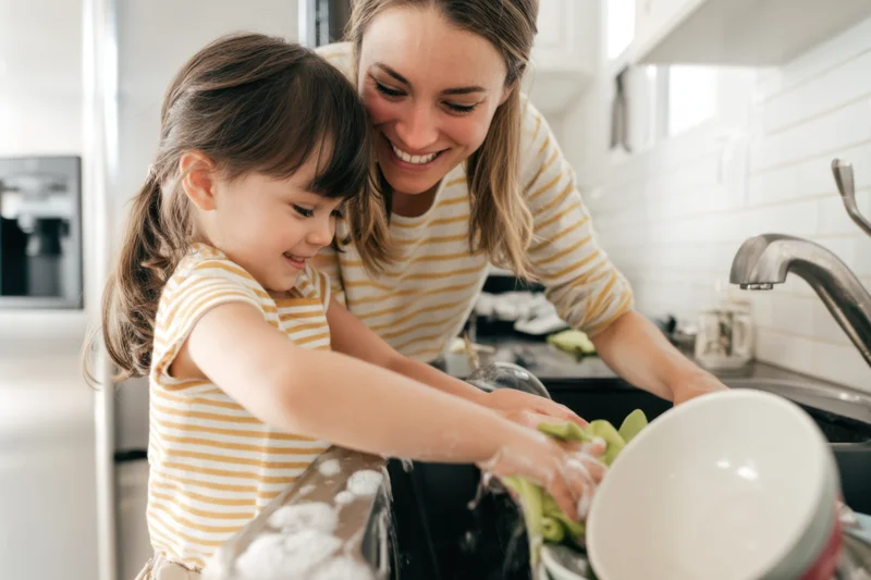 Woman and young girl washing dishes together at kitchen sink