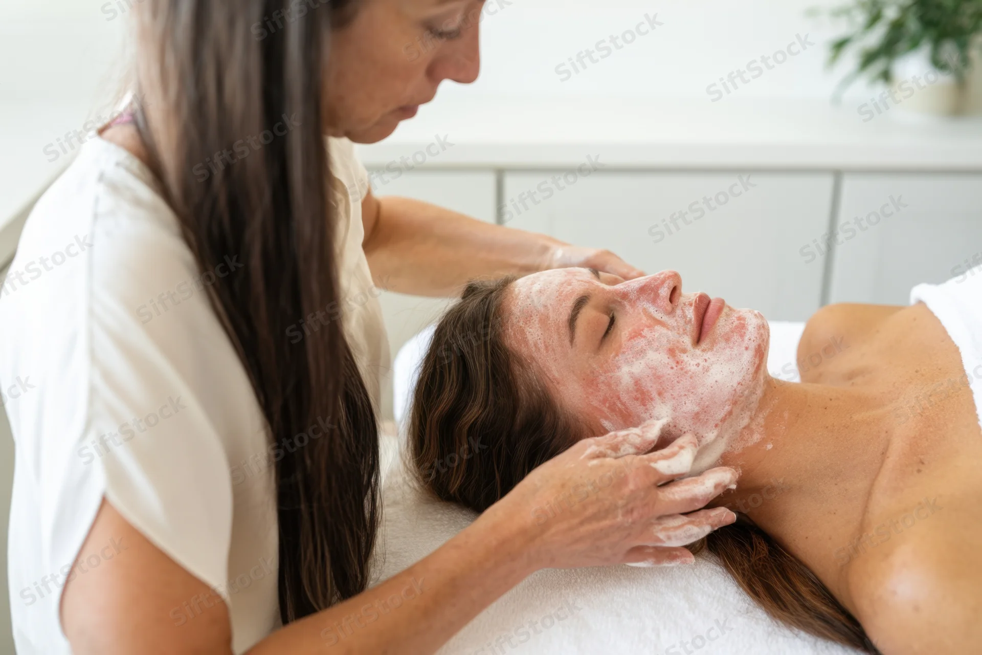 Woman receiving facial treatment with foamy exfoliant applied by therapist in spa setting
