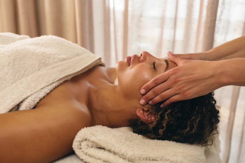 Woman receiving facial massage on spa table with eyes closed