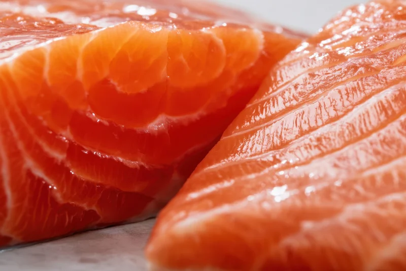 Close-up of raw salmon fillet showing orange flesh with white marbling on a light surface