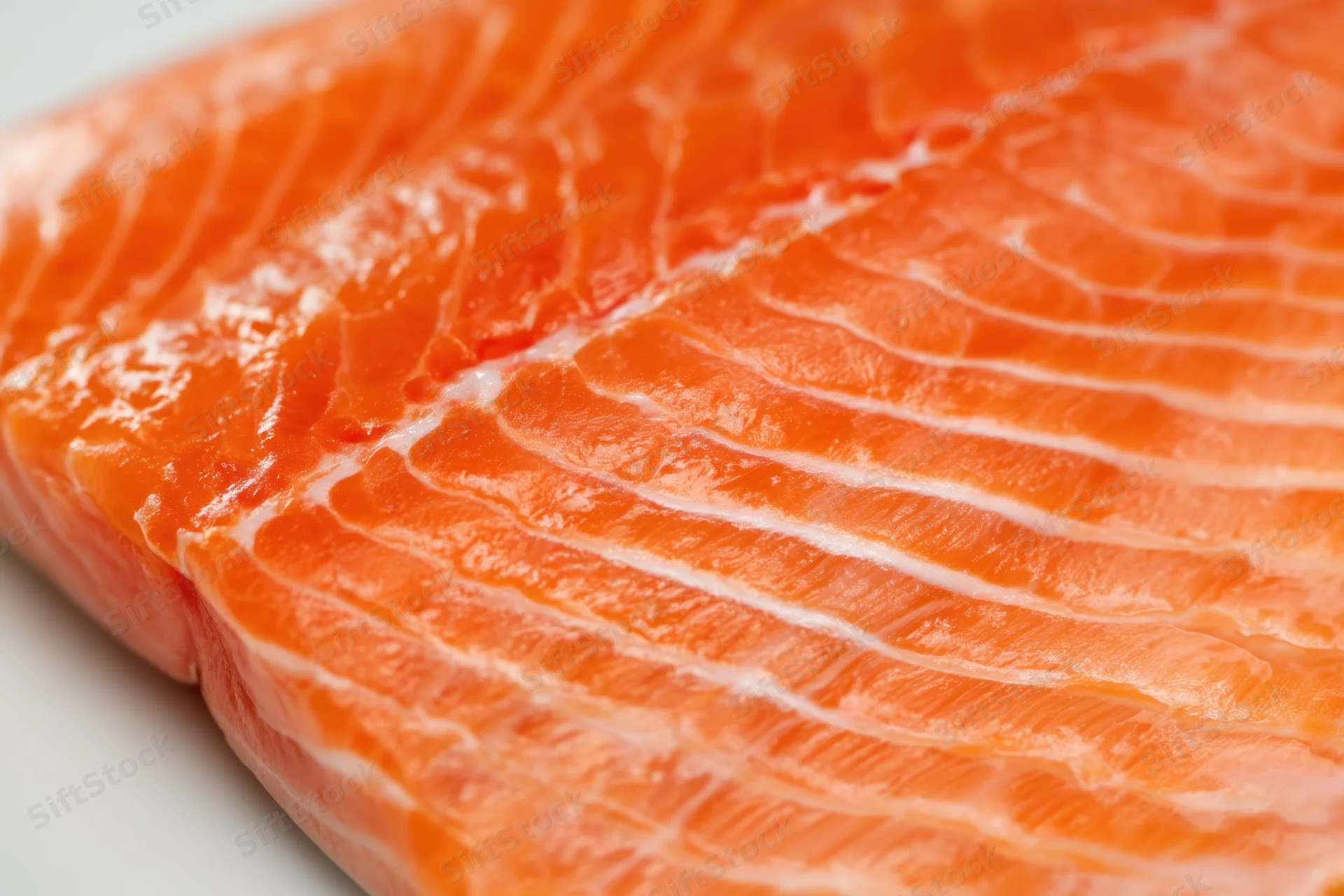 Close-up of a raw salmon fillet showing orange flesh with white marbling on a plain surface