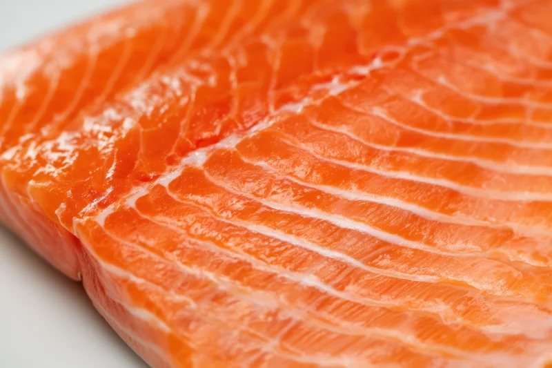 Close-up of a raw salmon fillet showing orange flesh with white marbling on a plain surface