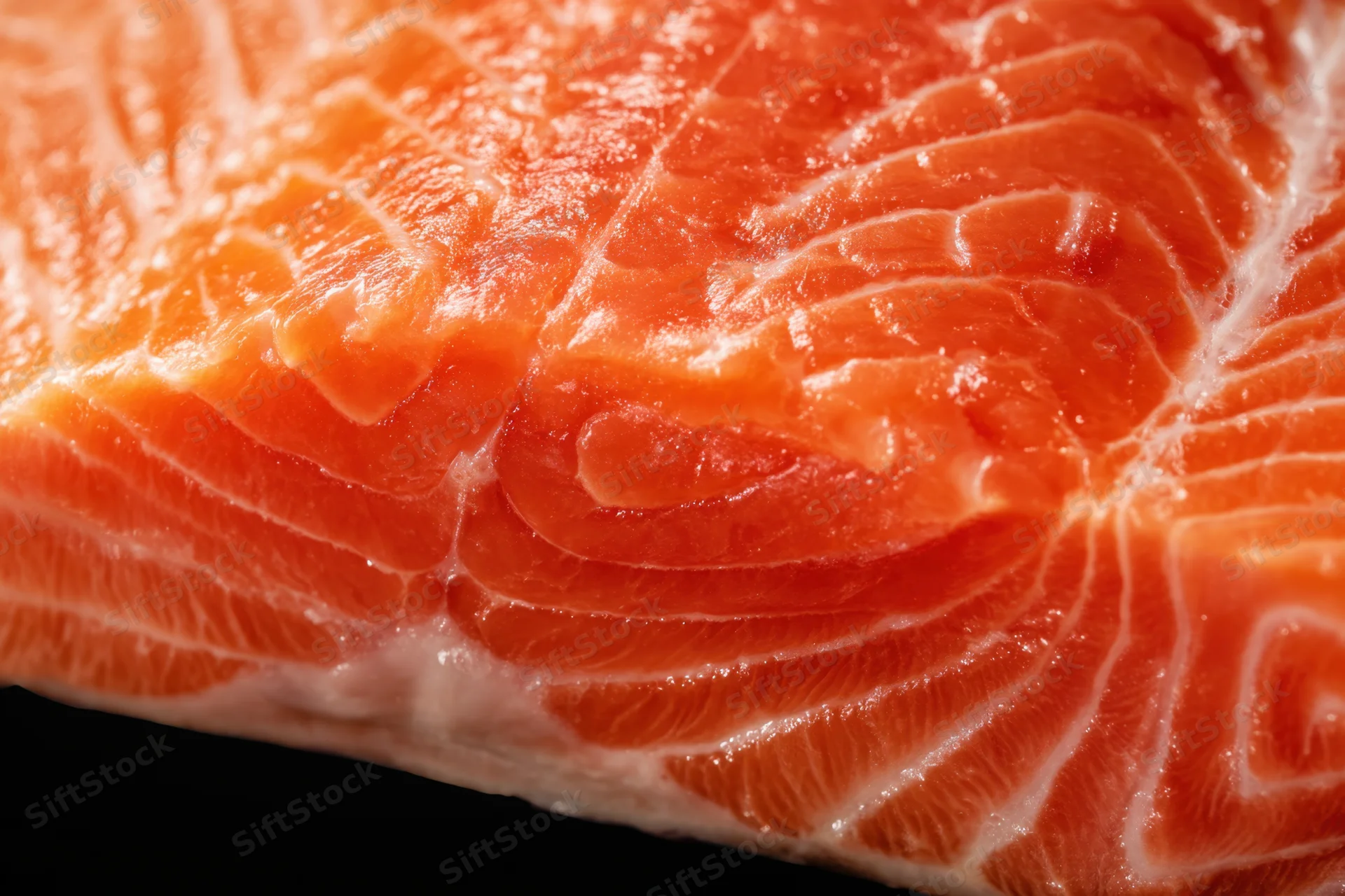 Close-up of a raw salmon fillet showing orange flesh and white marbling against black background