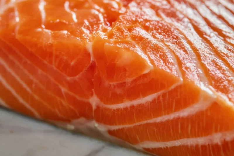 Close-up of a raw salmon fillet showing orange flesh with white marbling on a marble surface